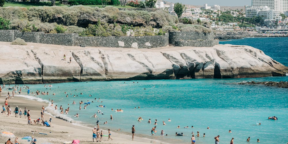 Busy Playa del Duque beach with swimmers and managed facilities in Costa Adeje