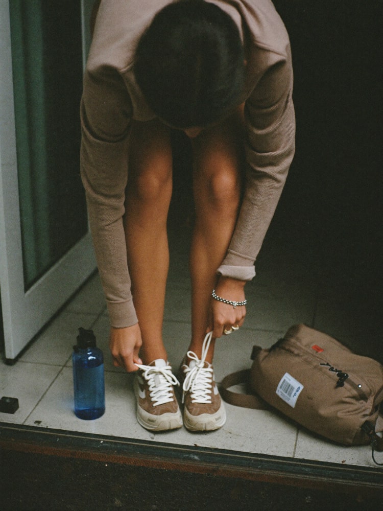 A person tying walking shoes beside an open doorway