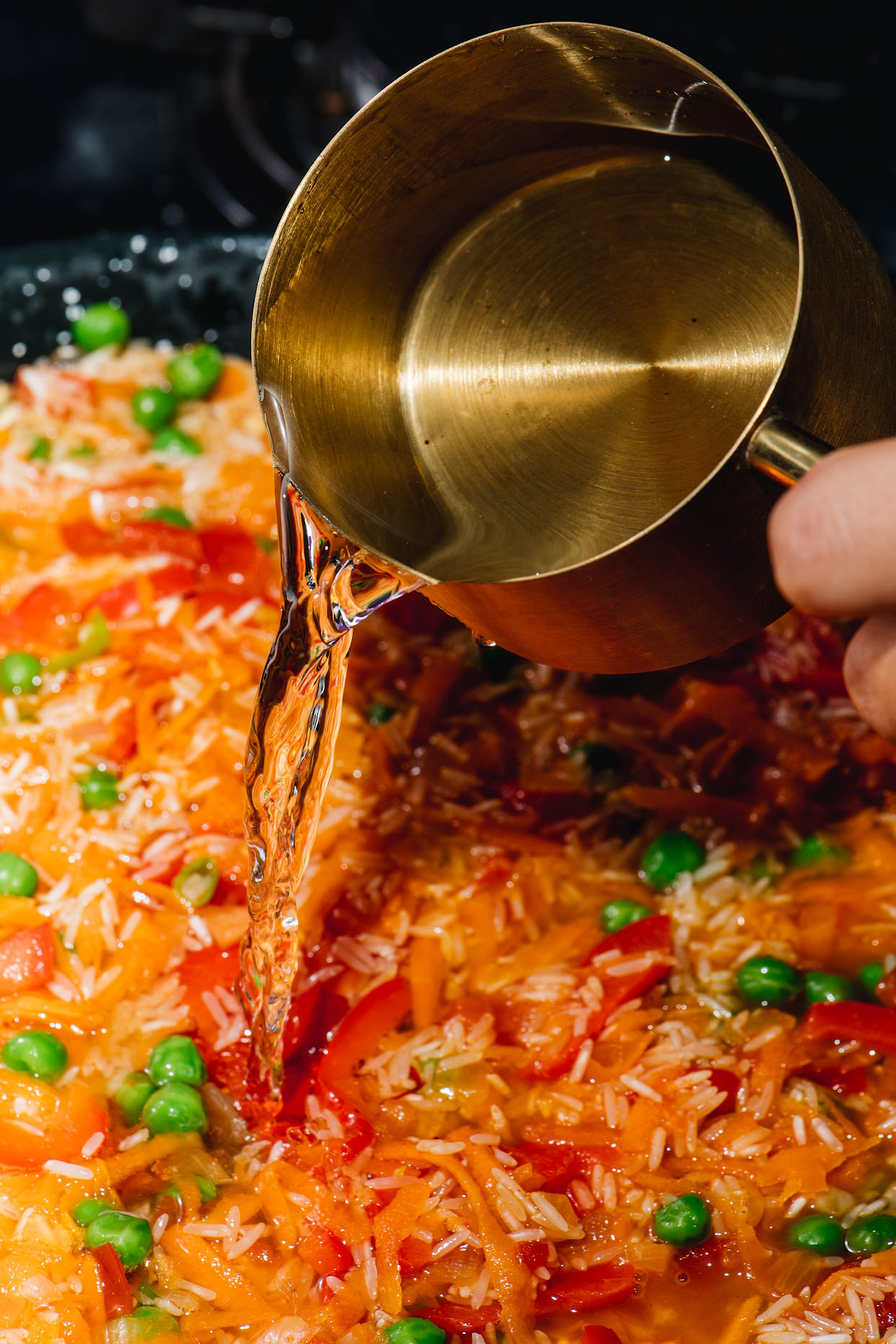 Hot stock poured into seafood paella rice with peas and peppers
