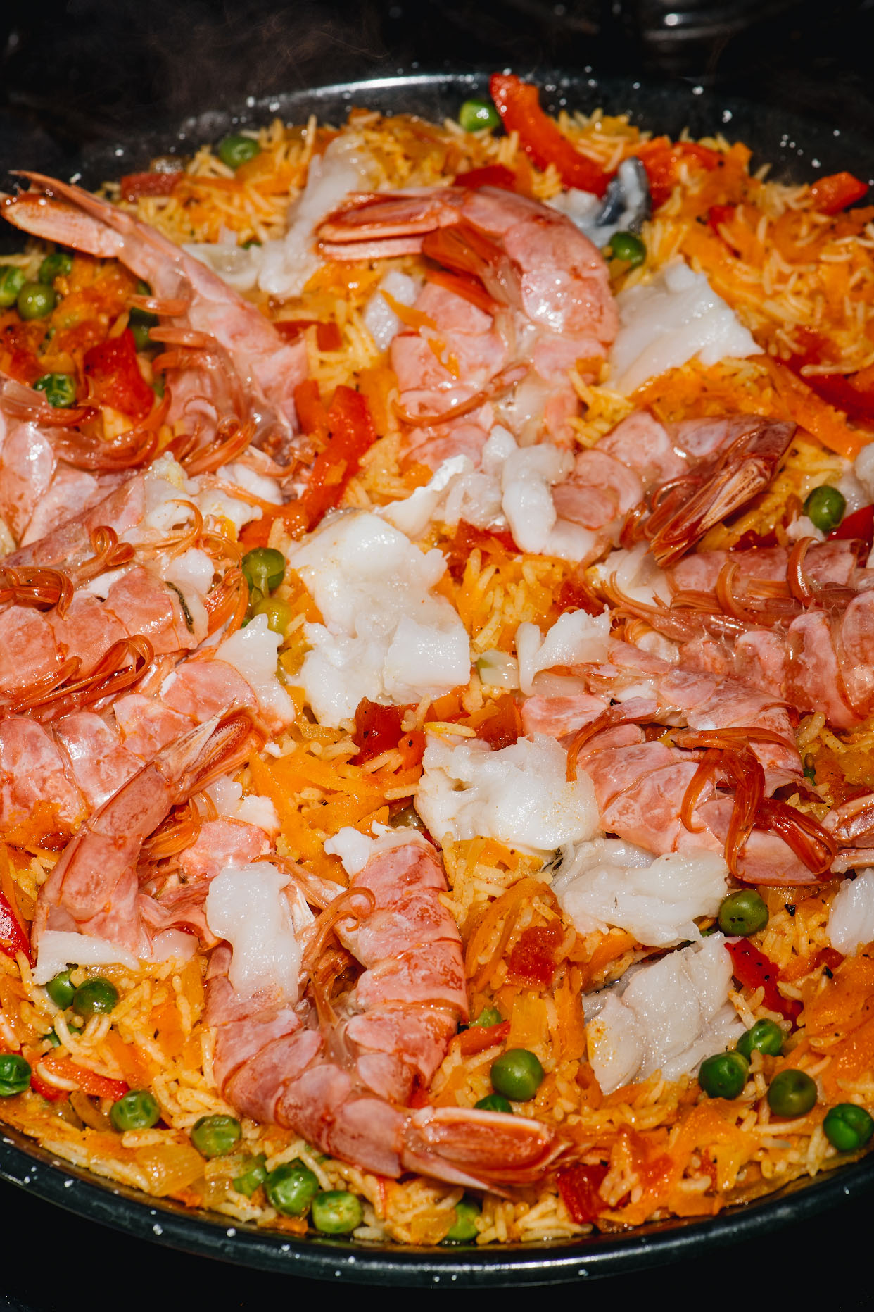 Raw prawns and white fish arranged over rice in a paella pan