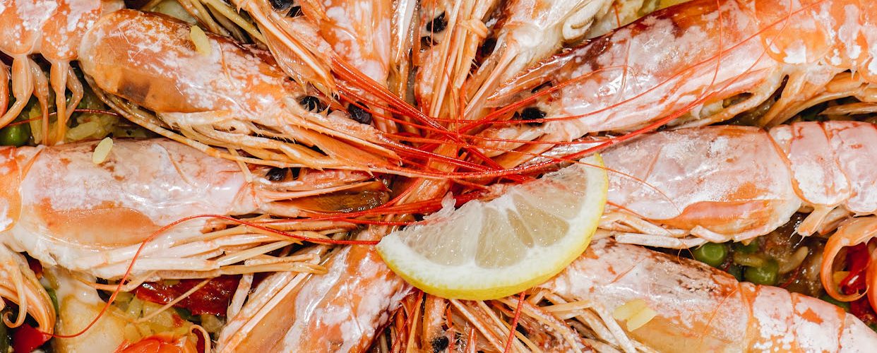 Seafood paella in a shallow pan topped with whole prawns and lemon