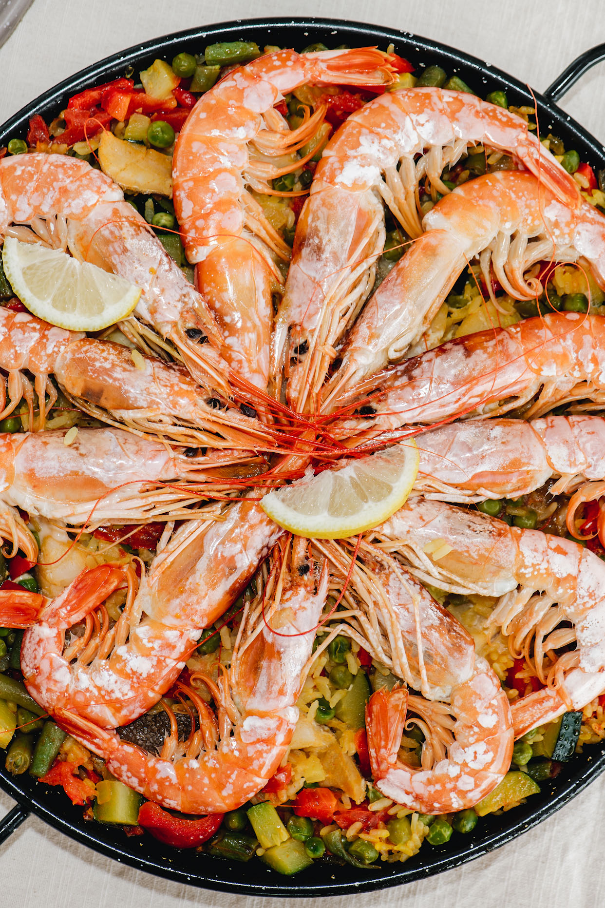 Seafood paella in a shallow pan topped with whole prawns and lemon