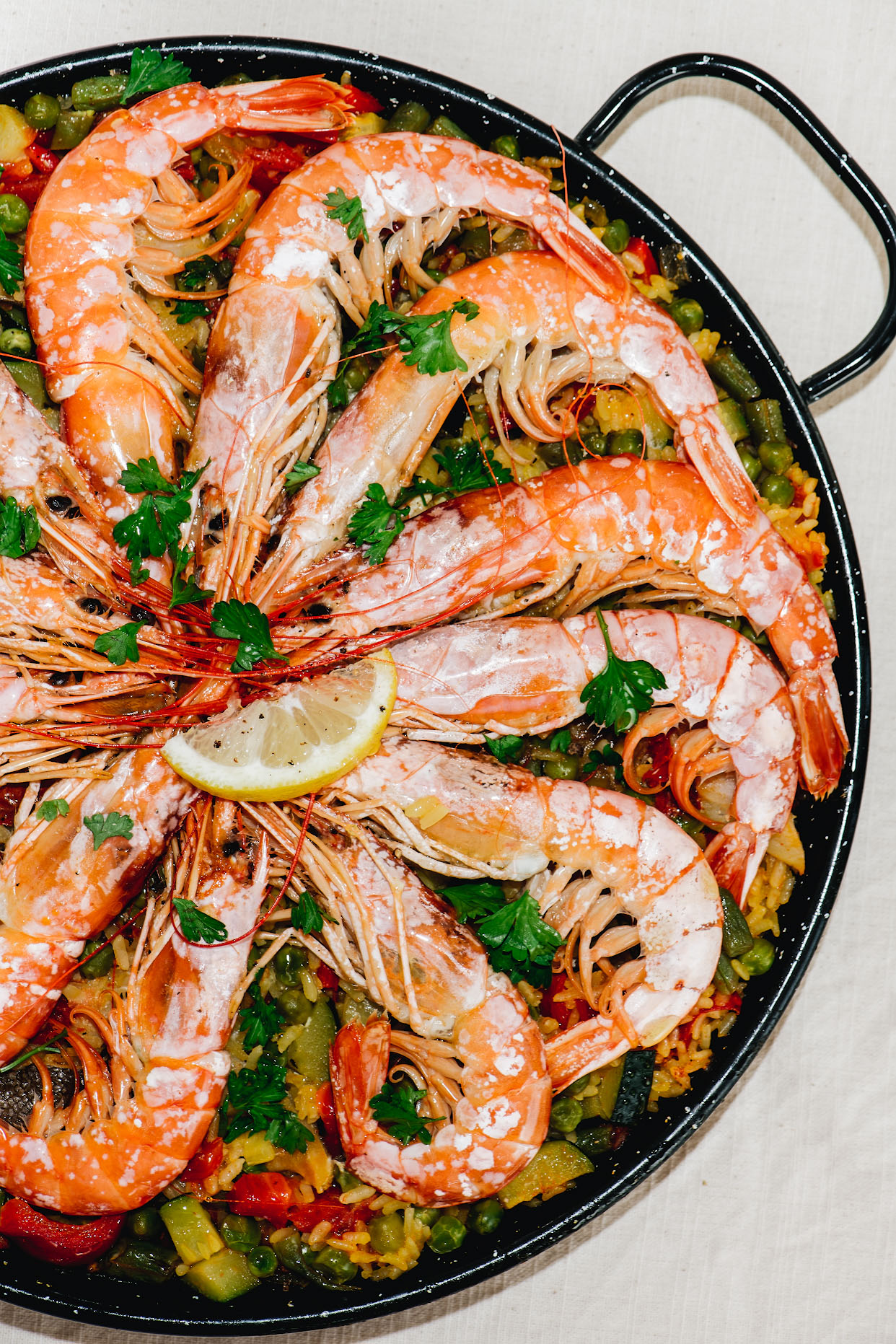 Whole prawns arranged over seafood paella in a black paella pan